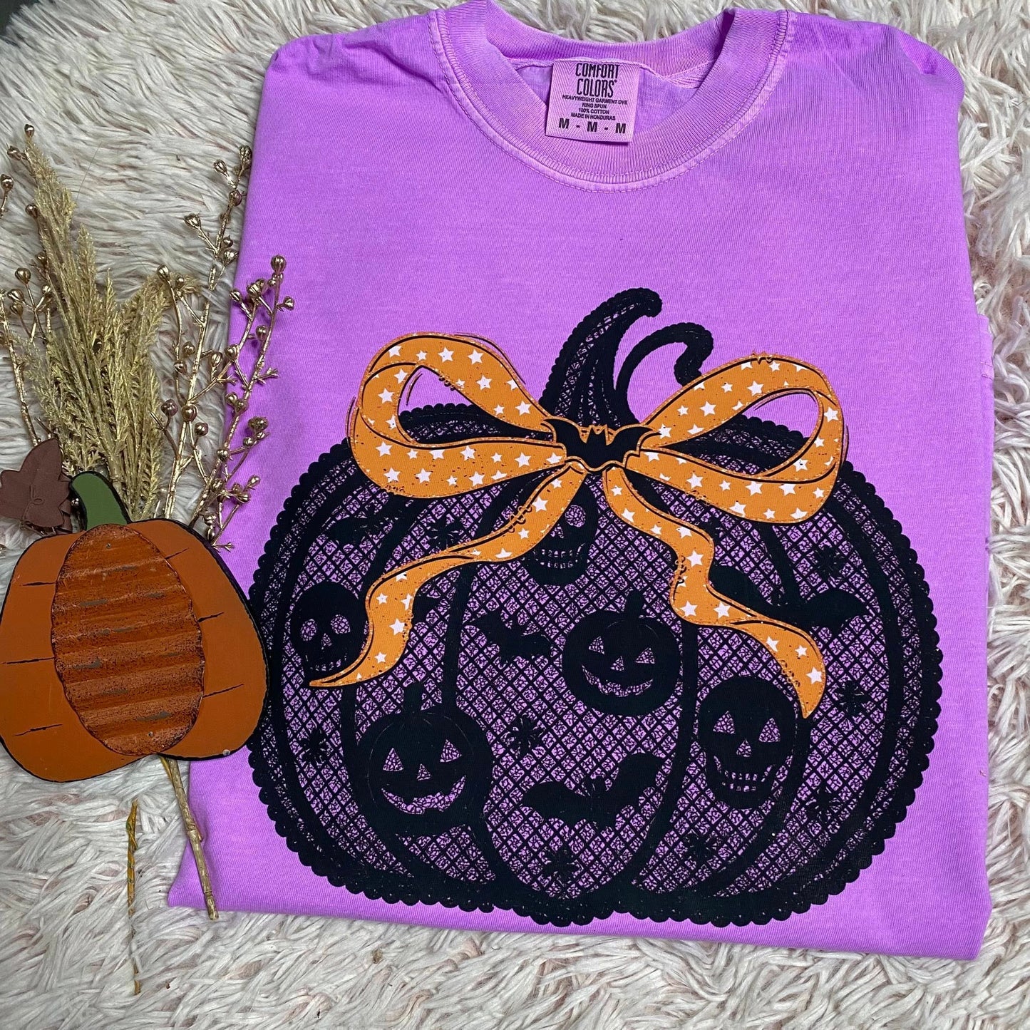 Purple shirt with a Halloween-themed design featuring a pumpkin and bow on a textured surface.