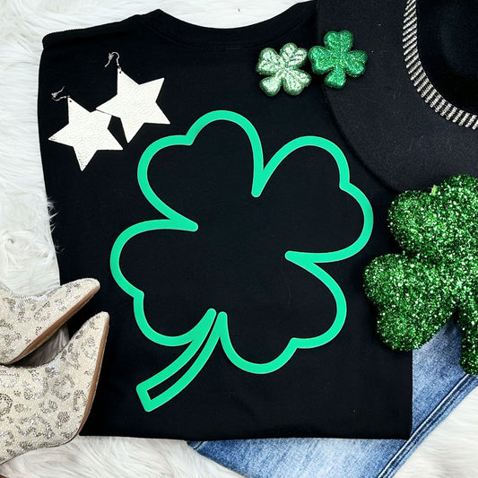 Black graphic tee featuring a large green puff outlined shamrock design, styled with glittery and festive St. Patrick’s Day accessories.