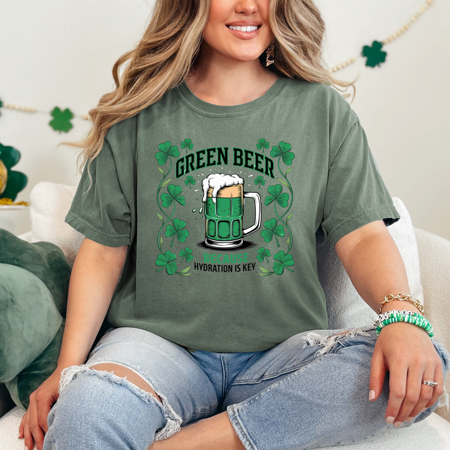 Moss green t-shirt featuring a fun design of a frothy mug of green beer surrounded by vibrant shamrocks. The text reads 'Green Beer - Because Hydration is Key,' making it a perfect choice for St. Patrick's Day celebrations with a humorous twist.