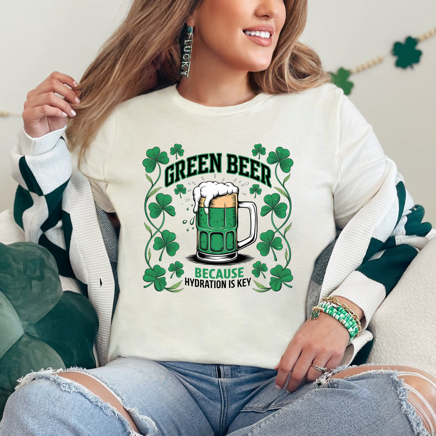 Natural-colored St. Patrick’s Day graphic tee featuring a mug of green beer surrounded by shamrocks with the text 'Green Beer, Because Hydration is Key.