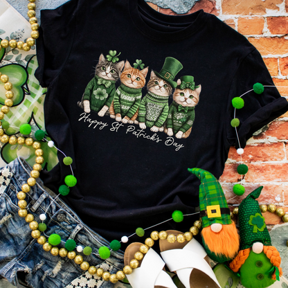 Heather black graphic tee featuring four cats in green St. Patrick’s Day outfits with shamrocks, leprechaun hats, and festive text.