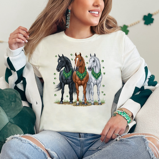 Natural-colored St. Patrick’s Day graphic tee featuring three horses wearing green shamrock bandanas with clover accents.