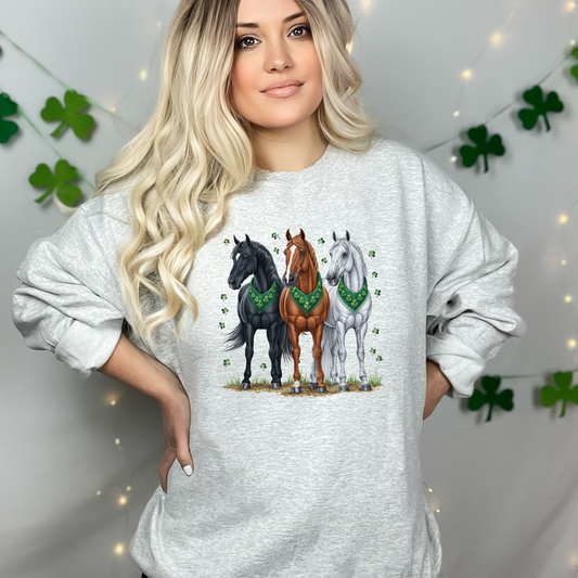 Heather gray sweatshirt showcasing a trio of elegant horses—black, chestnut, and white—dressed with green St. Patrick’s Day bandanas, surrounded by scattered shamrocks. A charming design perfect for horse lovers celebrating Irish luck.