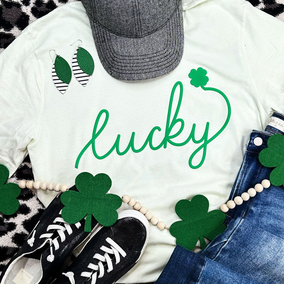 Light citron graphic tee featuring the word 'Lucky' in a green puff script with a shamrock accent, styled with casual and festive accessories.